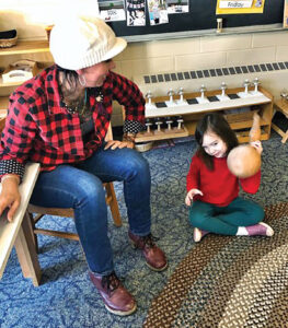 little girl in a red sweater shaking a squash and a woman sitting in a chair next to her